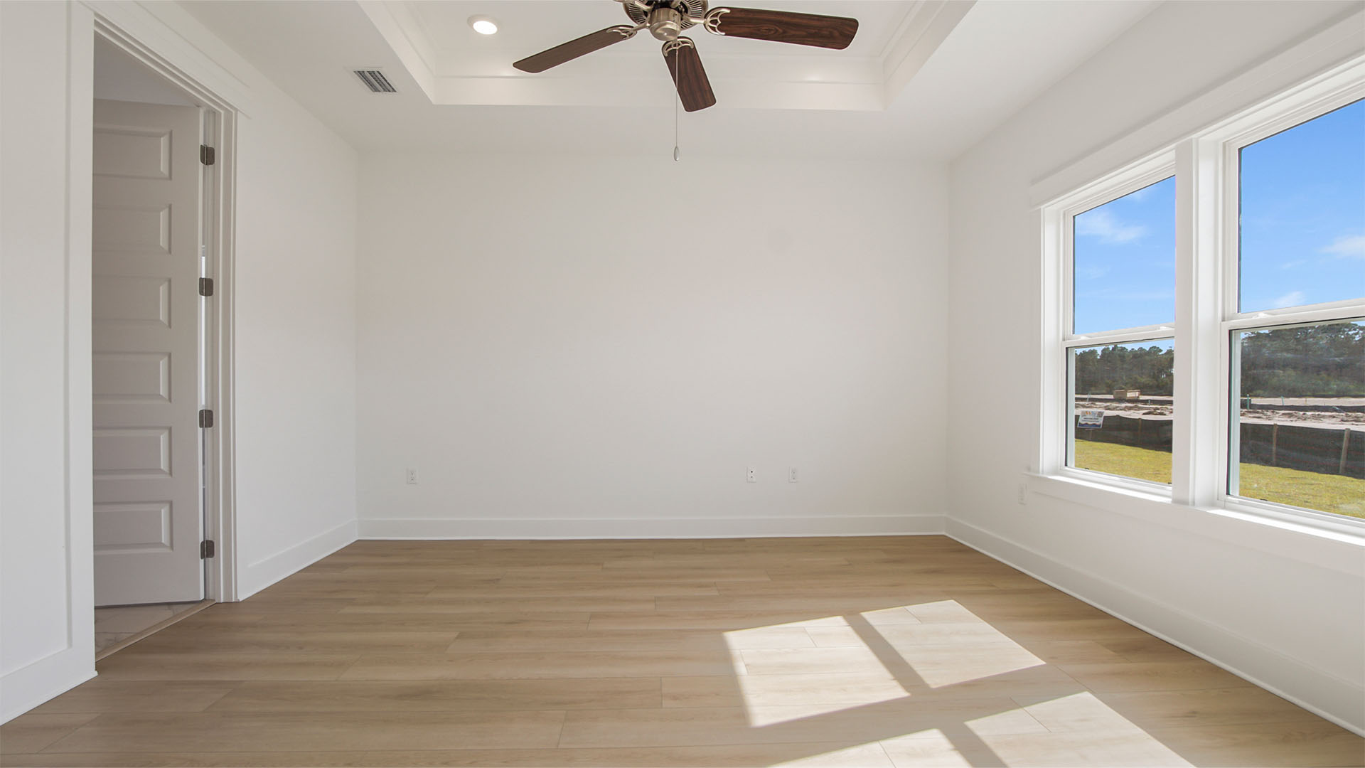 Primary bedroom with large windows and tall trey ceilings and ceiling fan and entrance to primary bedroom.