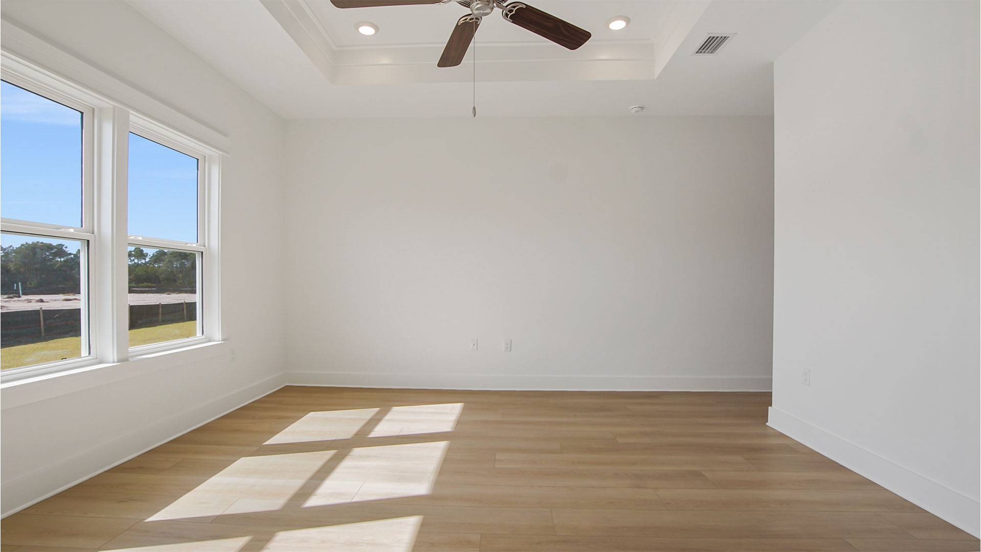 Primary bedroom with ceiling fan and tall trey ceilings and large windows and EVP flooring.