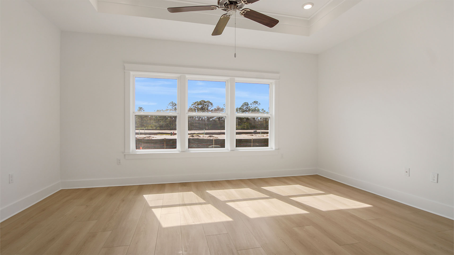 Primary bedroom with large windows and large windows and tall trey ceilings and ceiling fan.