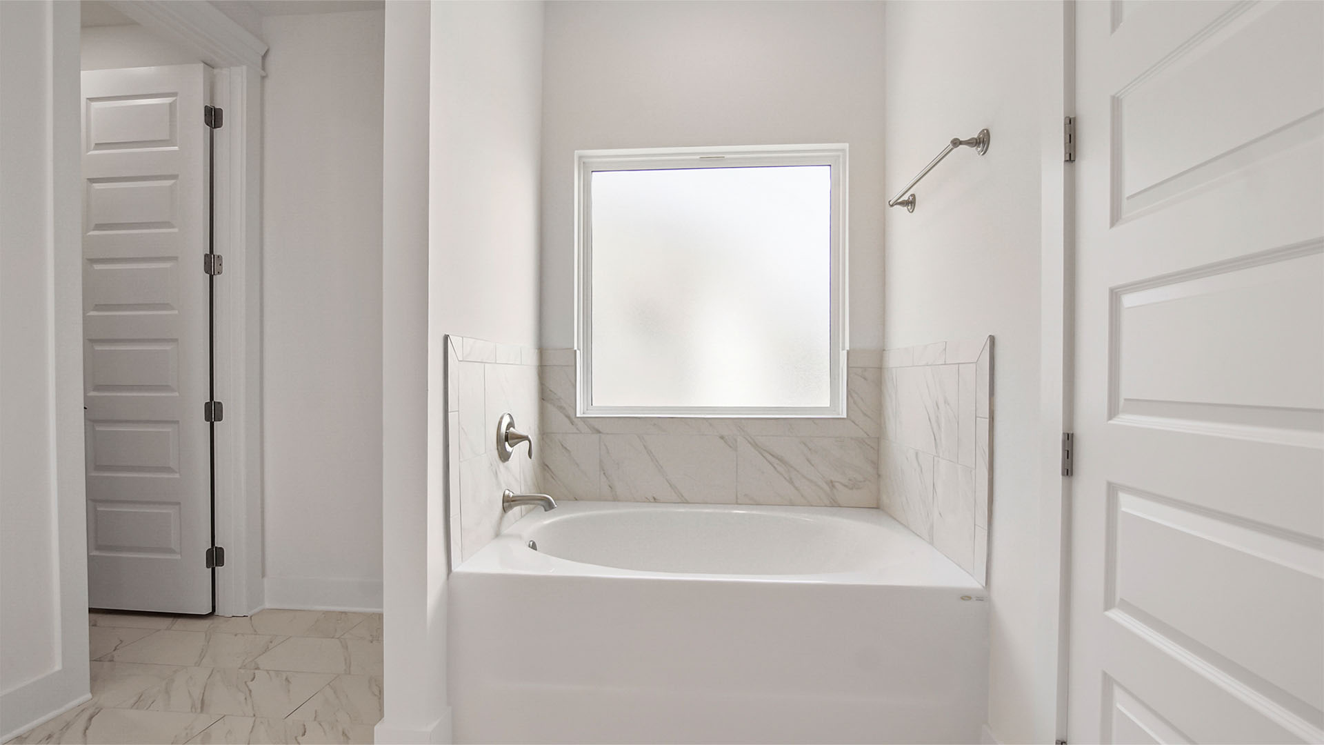 Primary bathroom with large soaking tub and marbled tile shower below frosted glass window.