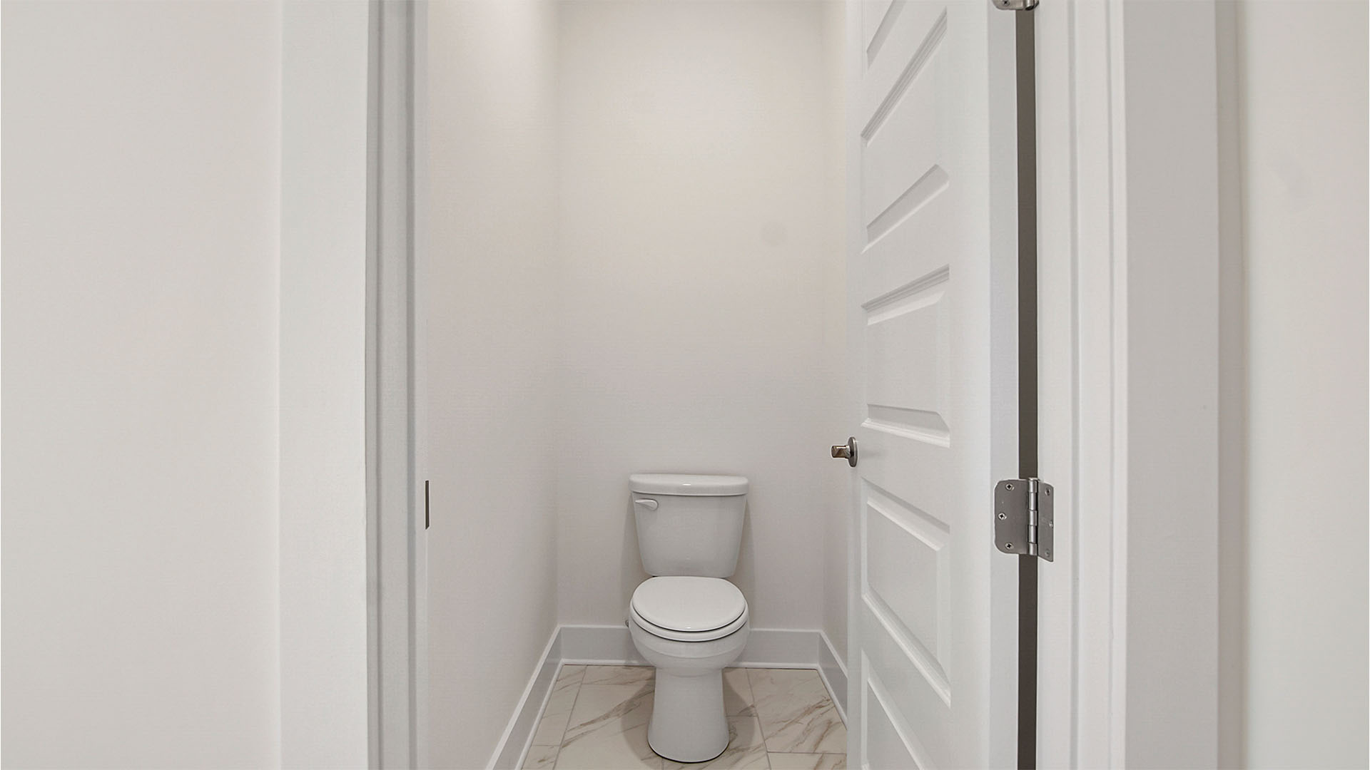 Water closet in primary bathroom with marbled tile flooring.