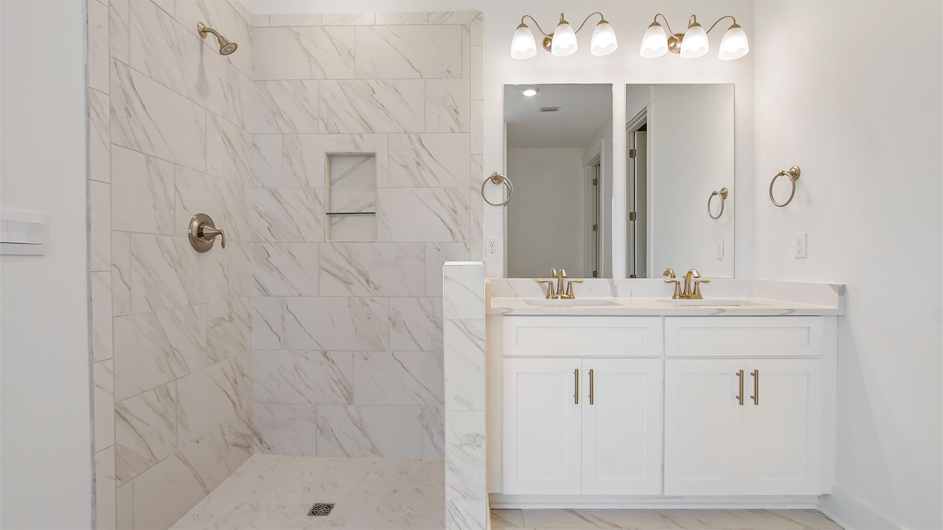 Primary bathroom with dual sink vanity with white cabinetry and quarts countertops and two mirrors and a zero-entry marbled tile shower.