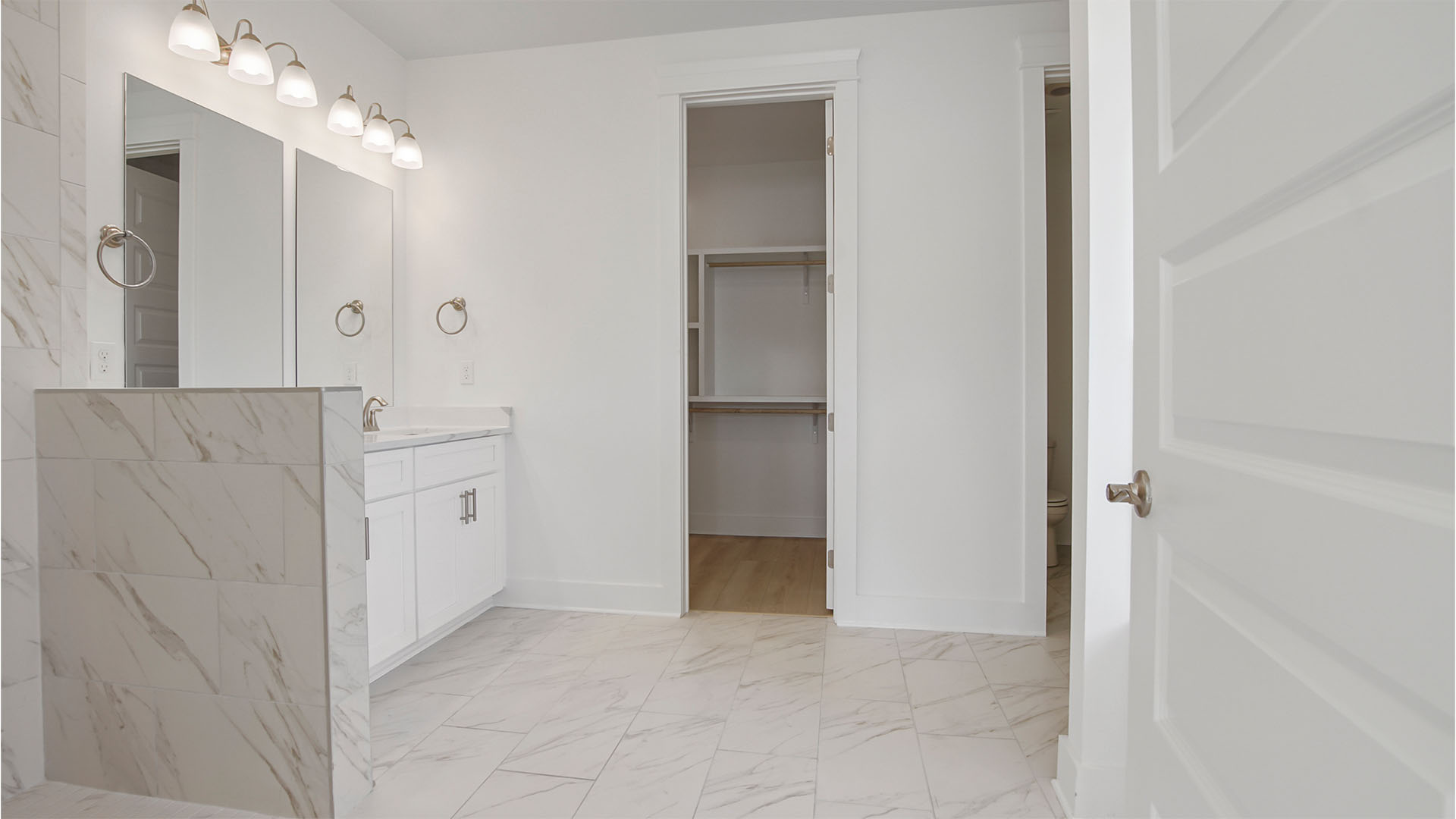 Primary bathroom with marbled tile flooring and walk-in closet and dual sink vanity with quartz countertops.