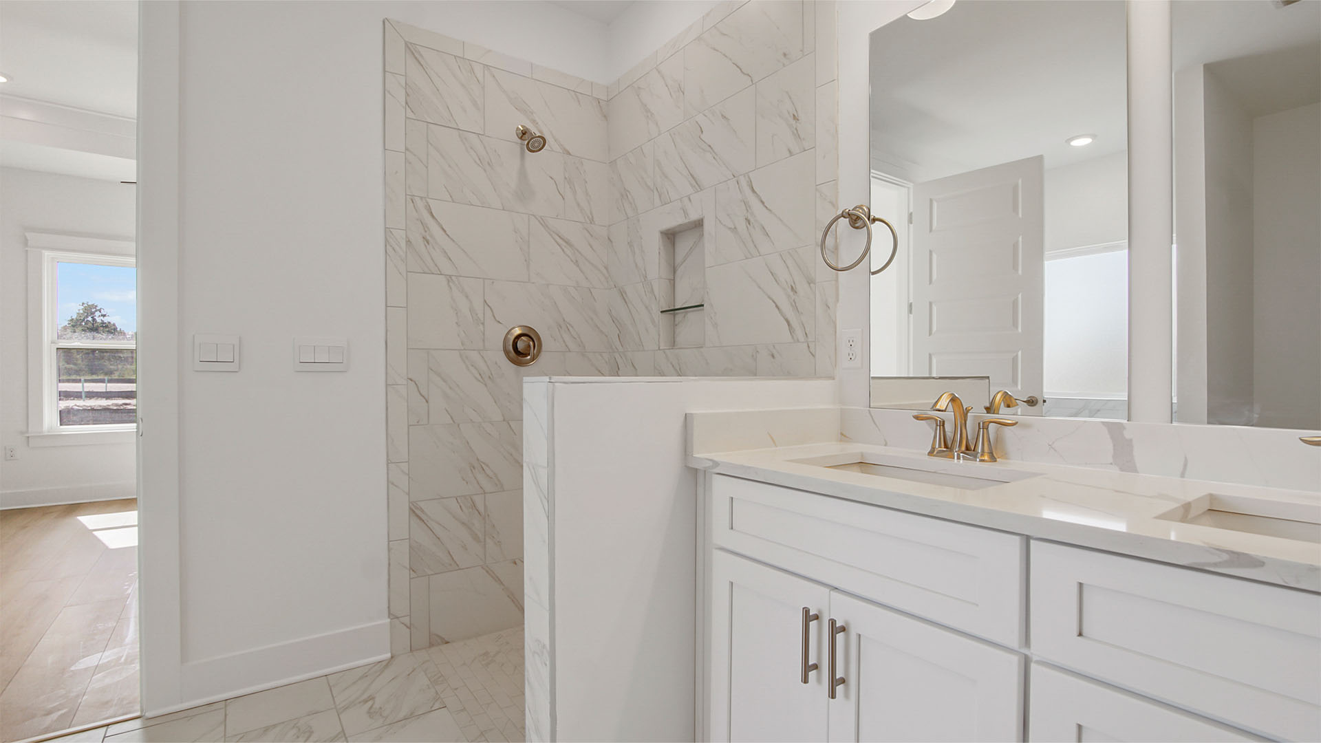 Primary bathroom with marbled tile zero entry shower and dual sink vanity with white cabinetry and quartz countertops.