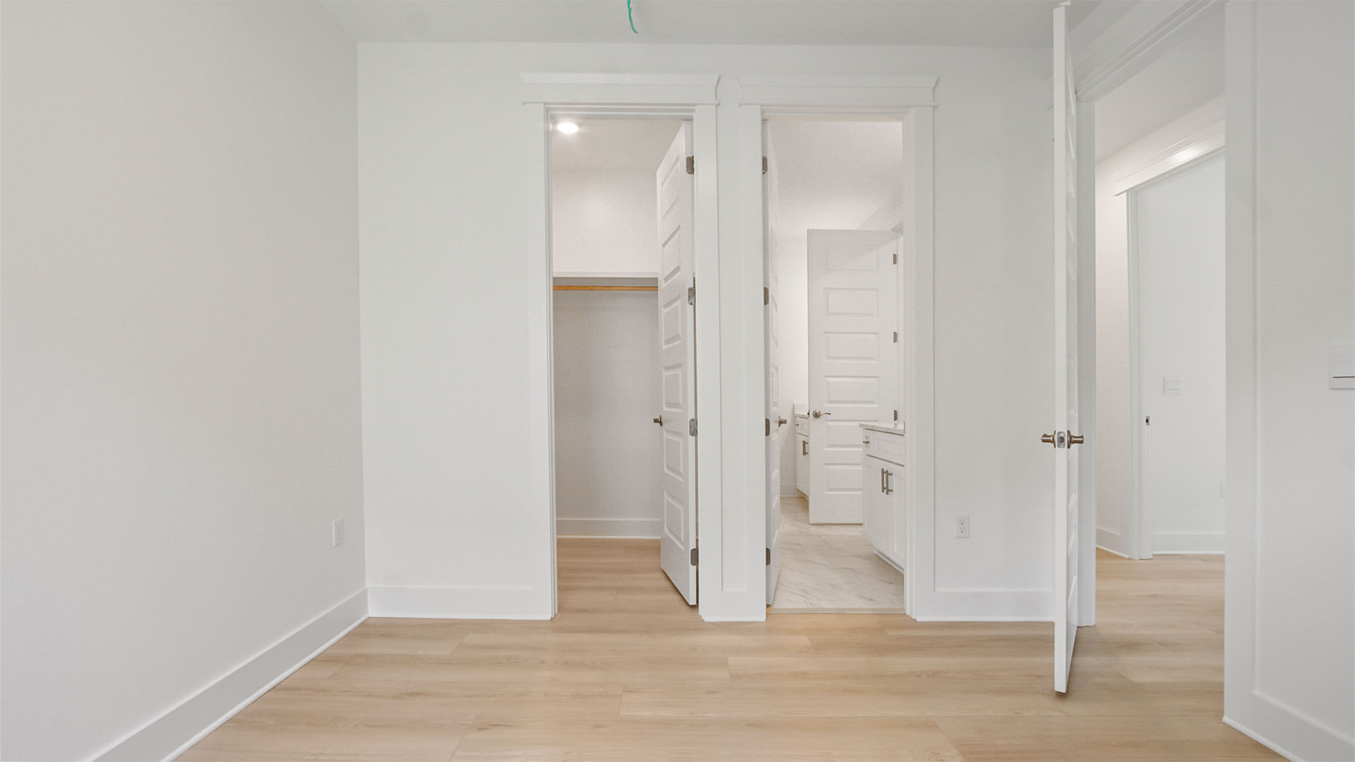 Bedroom four with EVP flooring and walk-in closet with wooden shelving and bathroom entrance.