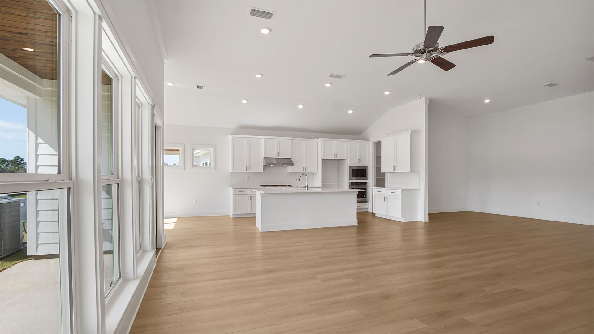 Open living area with large open kitchen with island and dining area and EVP flooring and large windows and back door to covered back patio.