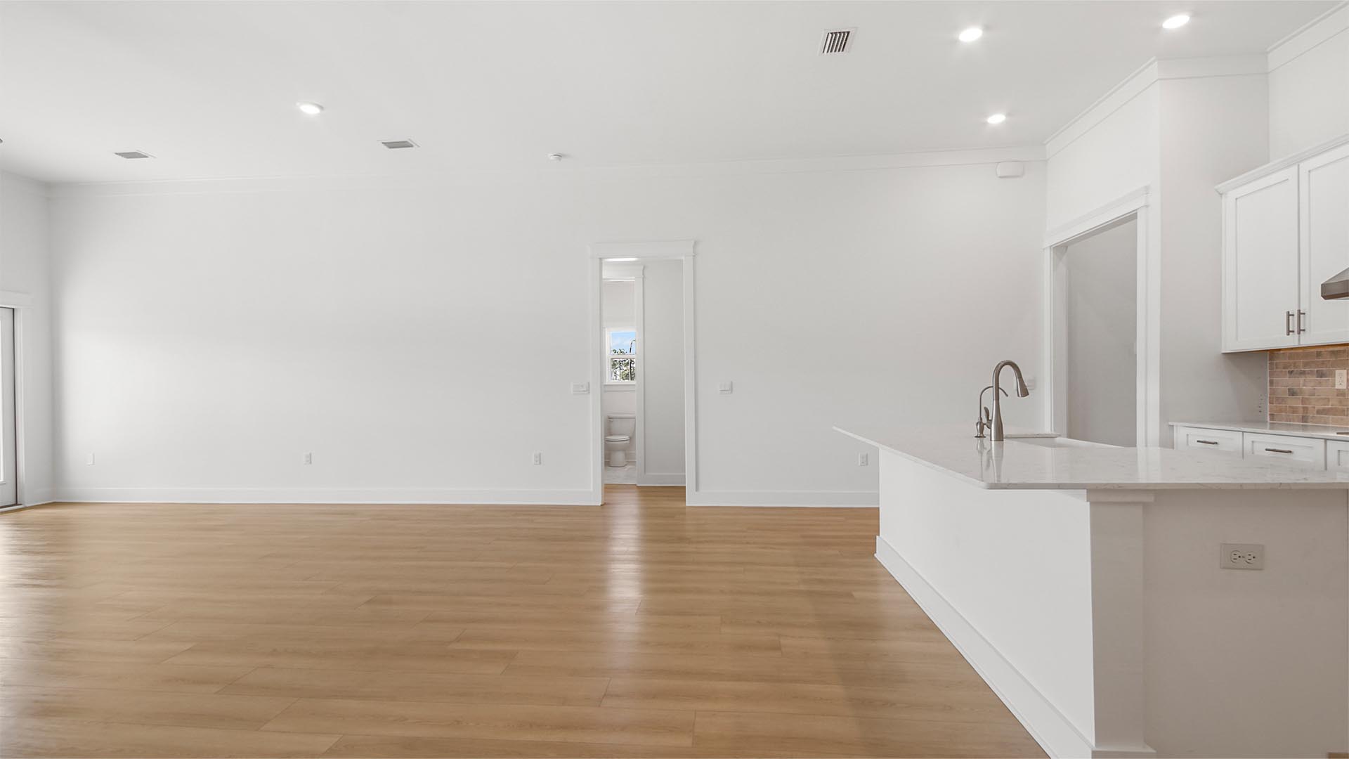 Bright open concept living area with large kitchen island overlooking living area and hallway to guest bedrooms and bathroom.