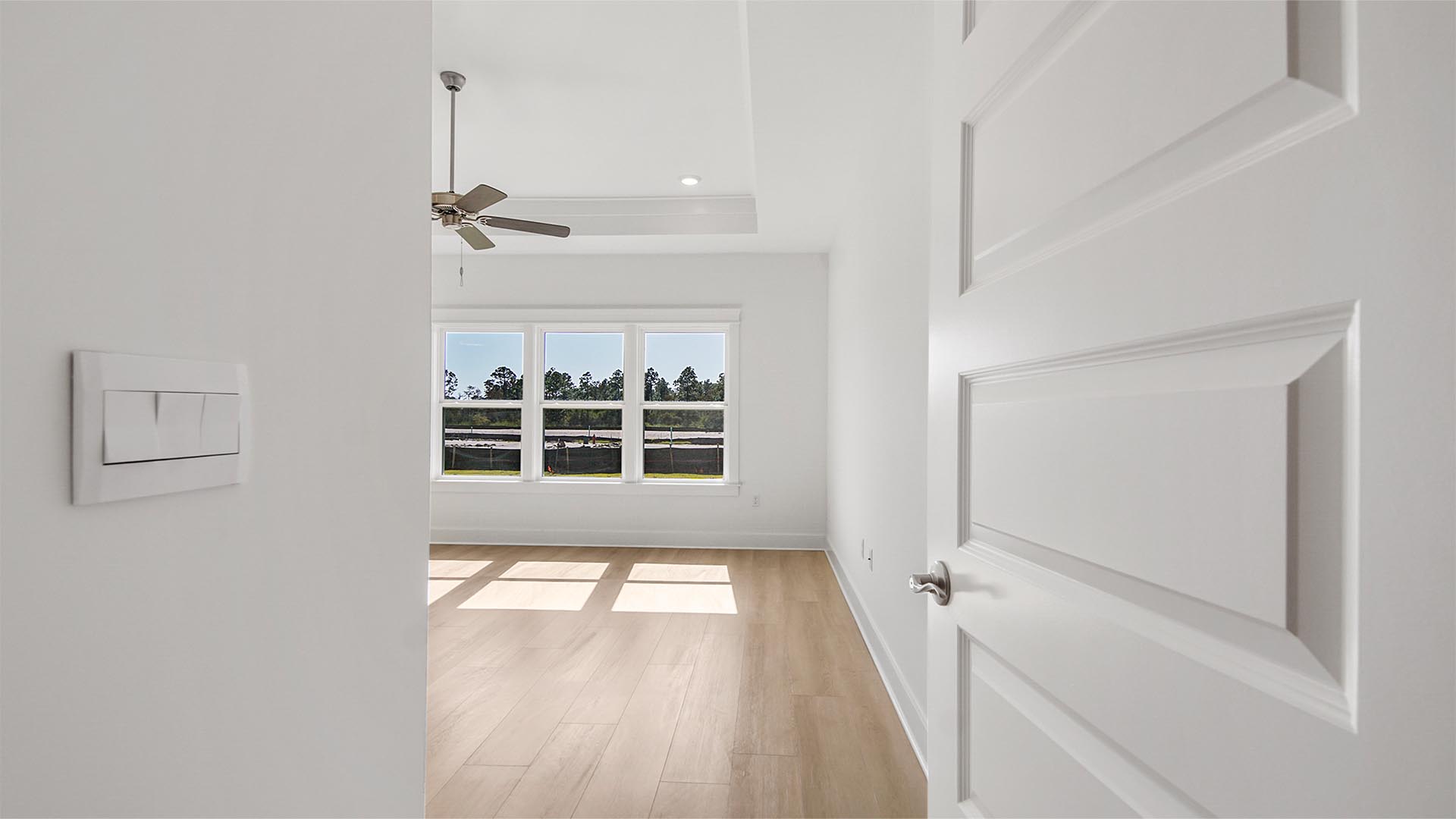 Private hallway to primary bedroom with EVP flooring and tray ceiling and large windows and ceiling fan.
