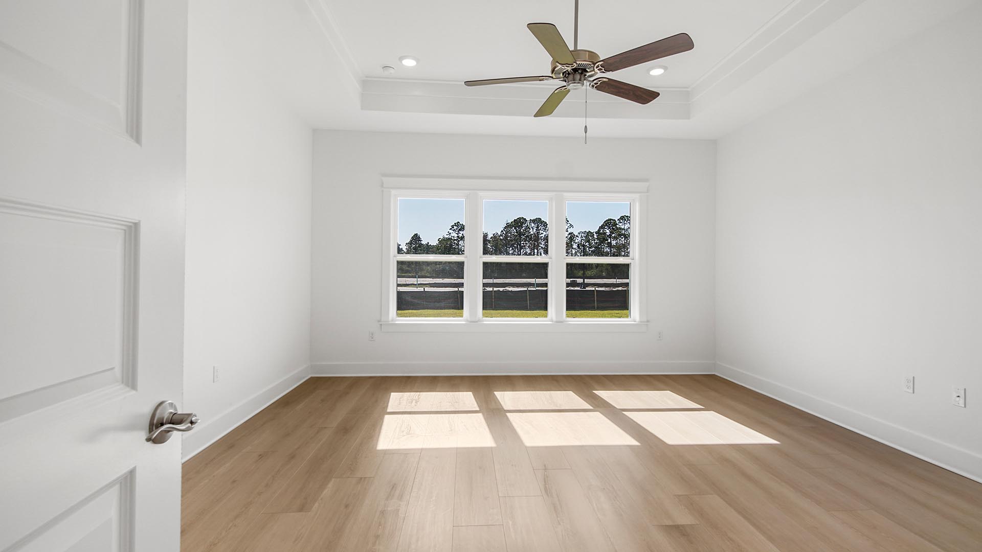 Brightly lit primary bedroom with large windows and EVP flooring and tray ceiling and ceiling fan.