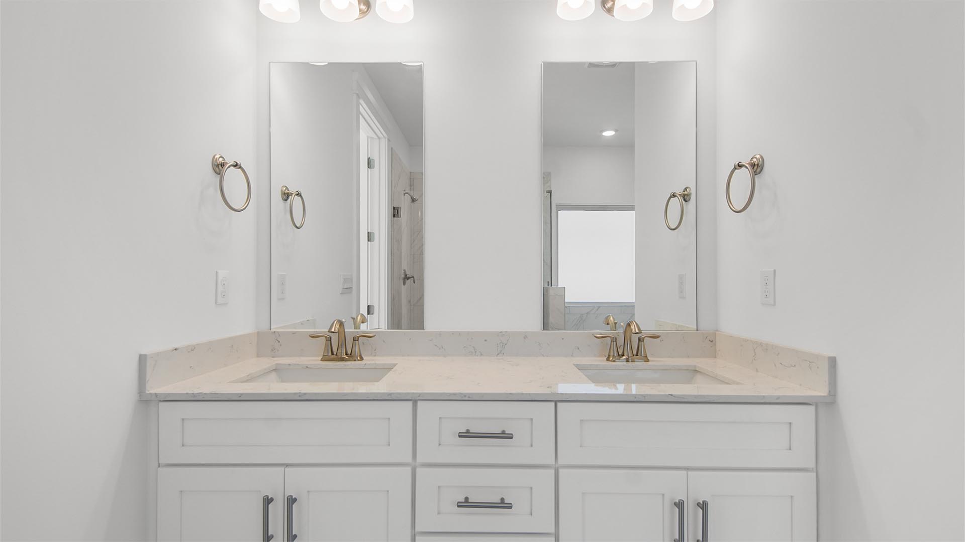 Primary bathroom with double sink vanity with quartz countertops and white cabinetry and two mirrors.