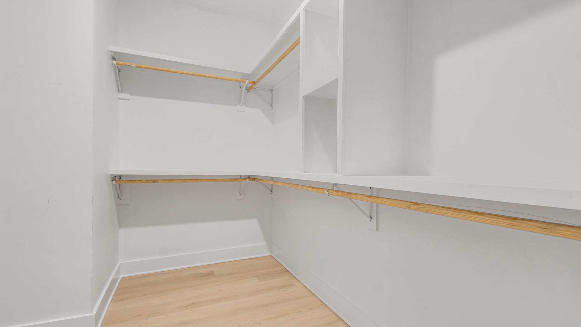 Large walk-in primary closet with wooden shelving and EVP flooring.