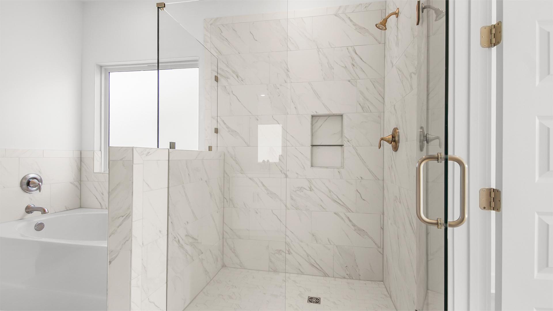 Oversized primary shower with marbled tile and glass doors.