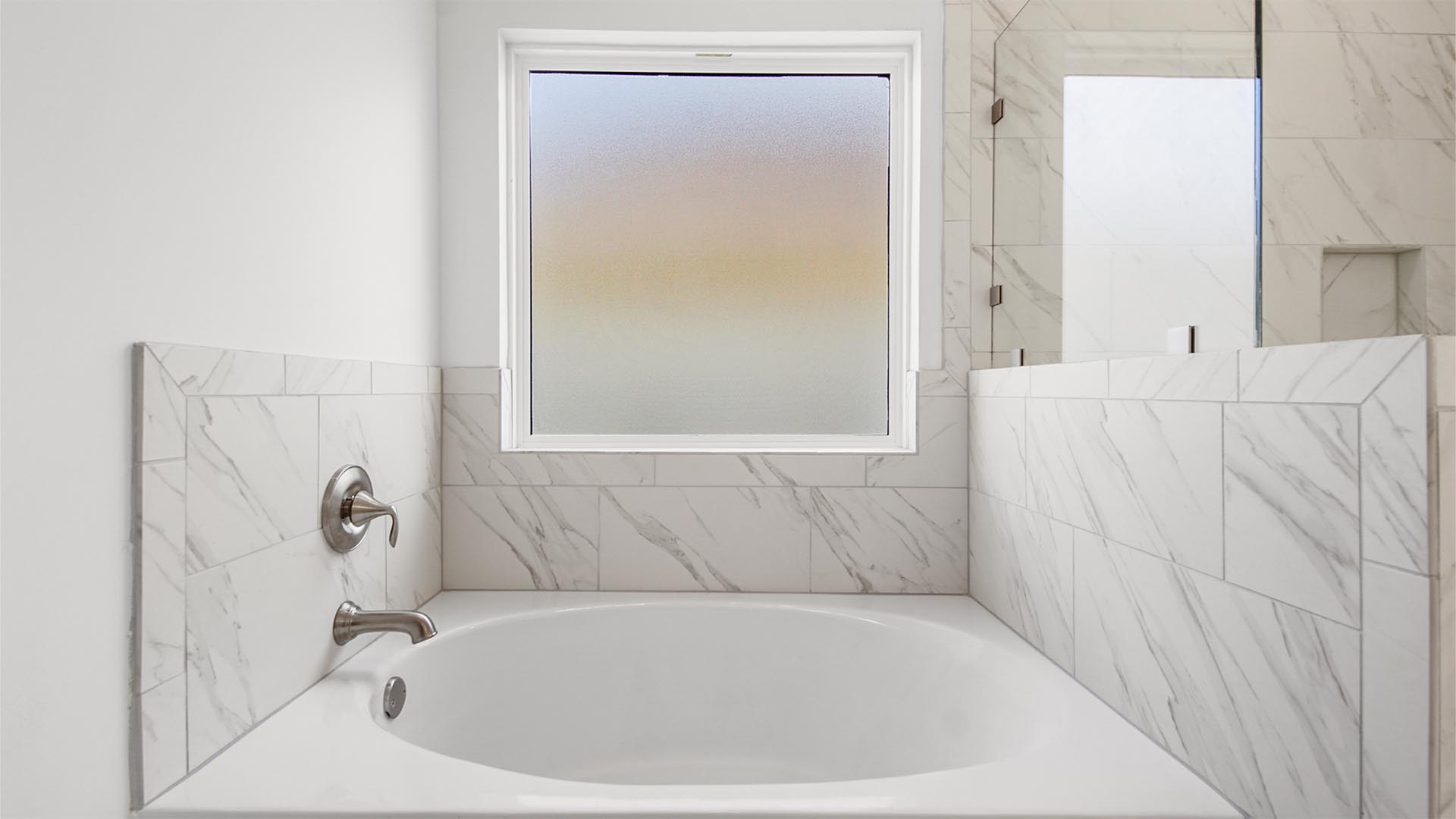 Large soaking tub with marbled tile backsplash beneath a frosted glass window.
