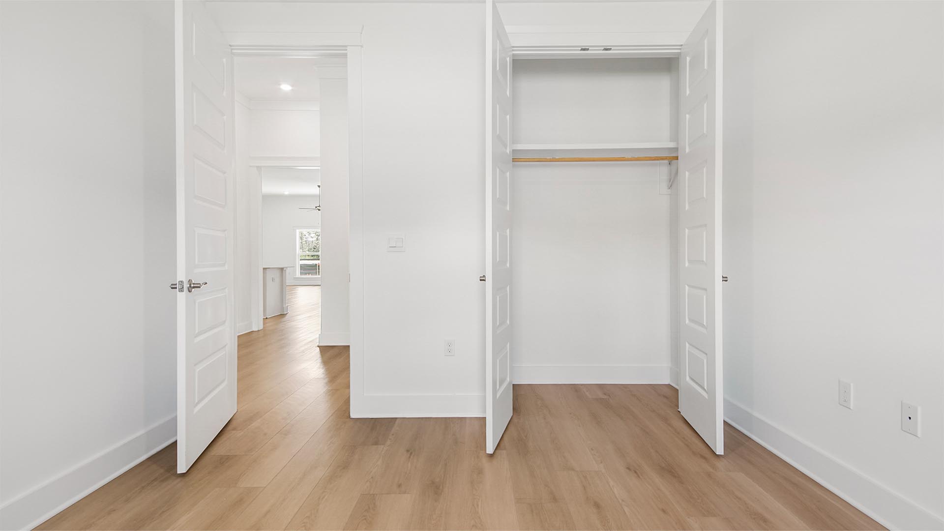 Bedroom two with EVP flooring and tall ceilings and double doors to closet with wooden shelving.