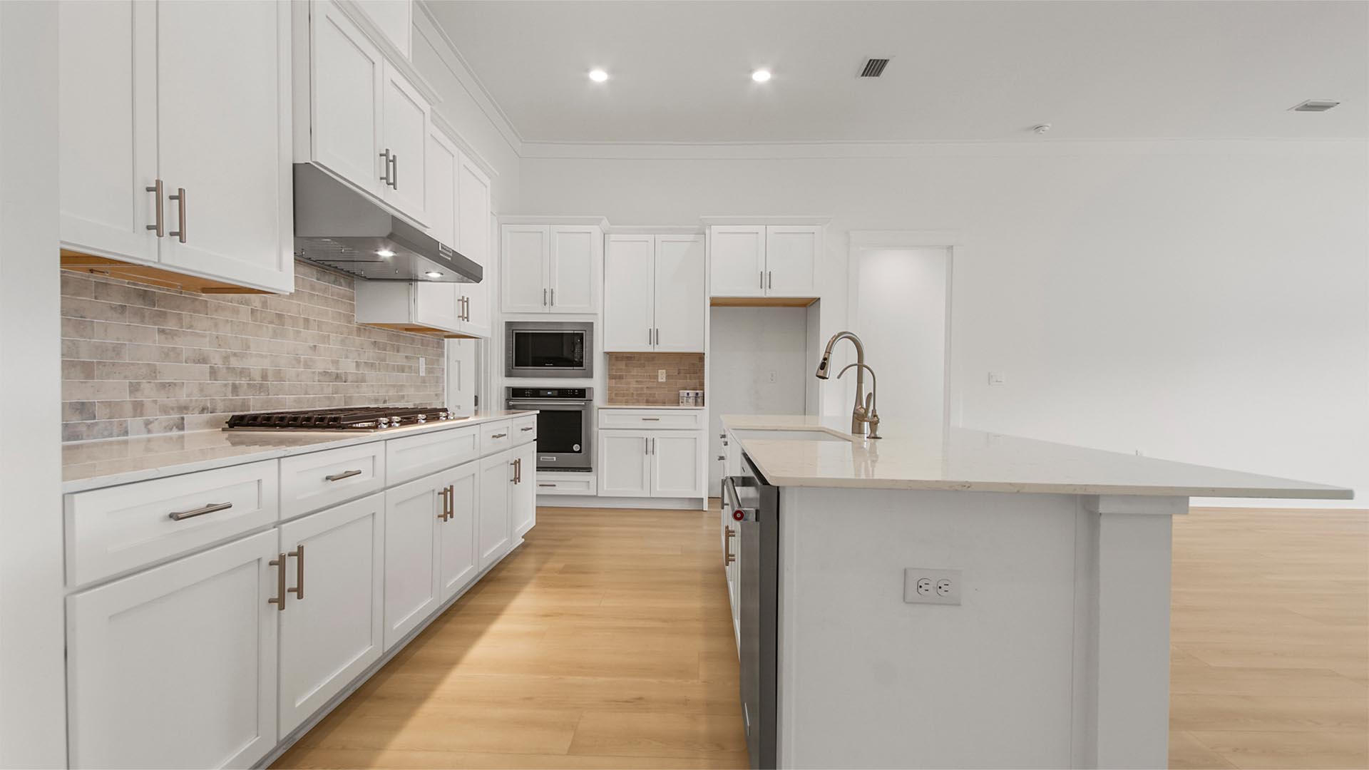 Open kitchen with large island and single basin undermount sink and white cabinetry and quartz countertops and Herringbone backsplash.