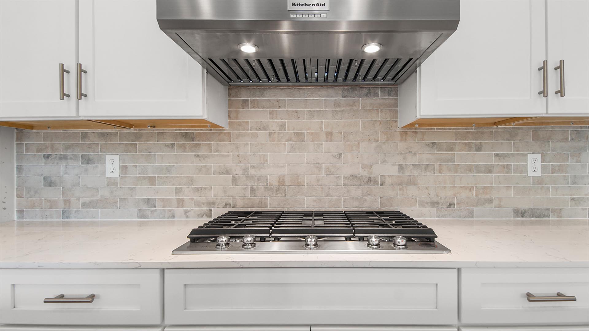 Gas burning stove and stainless-steel range hood and quartz countertops and Herringbone backsplash.
