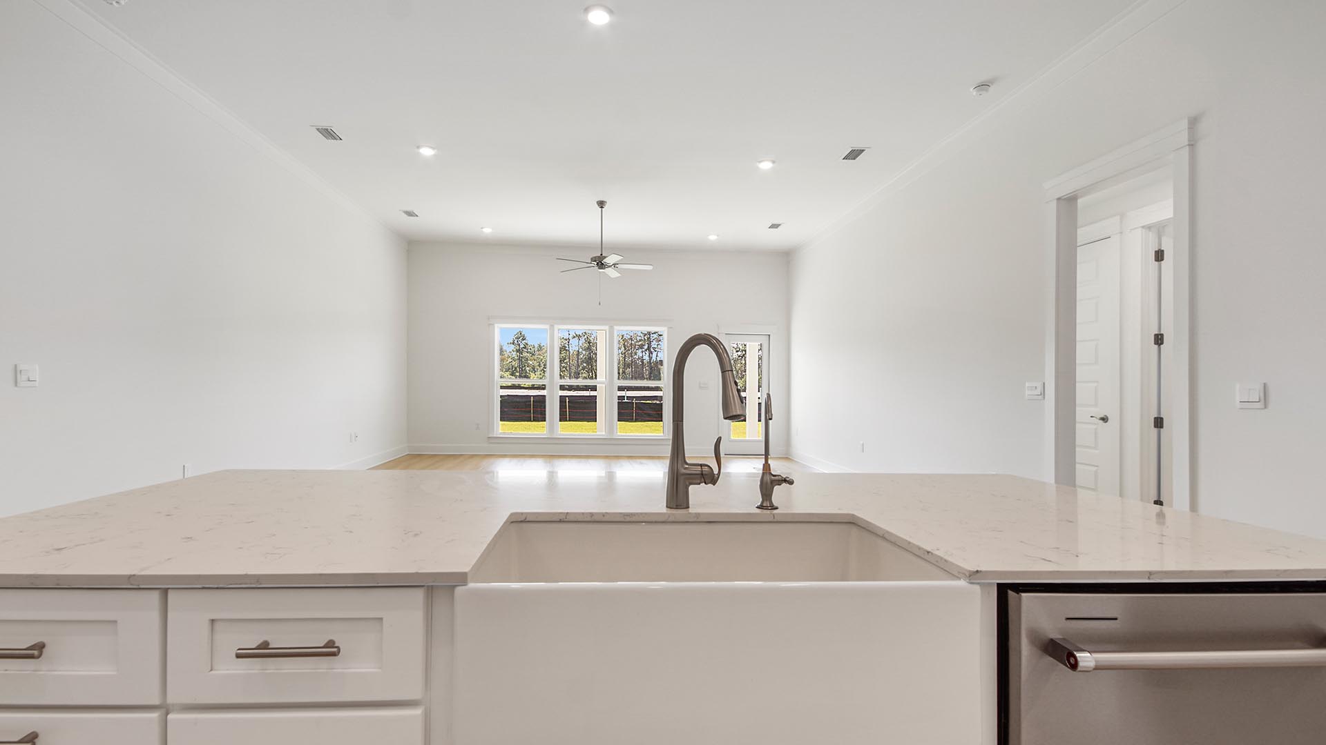 Large kitchen island overlooking open living area with large windows and island holding single basin undermount sink and stainless-steel dishwasher with hidden controls.