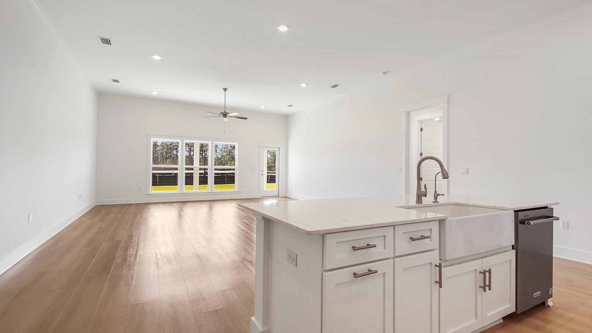 Open concept living area with large kitchen island overlooking living area with large windows and tall ceilings and door to cover back patio.