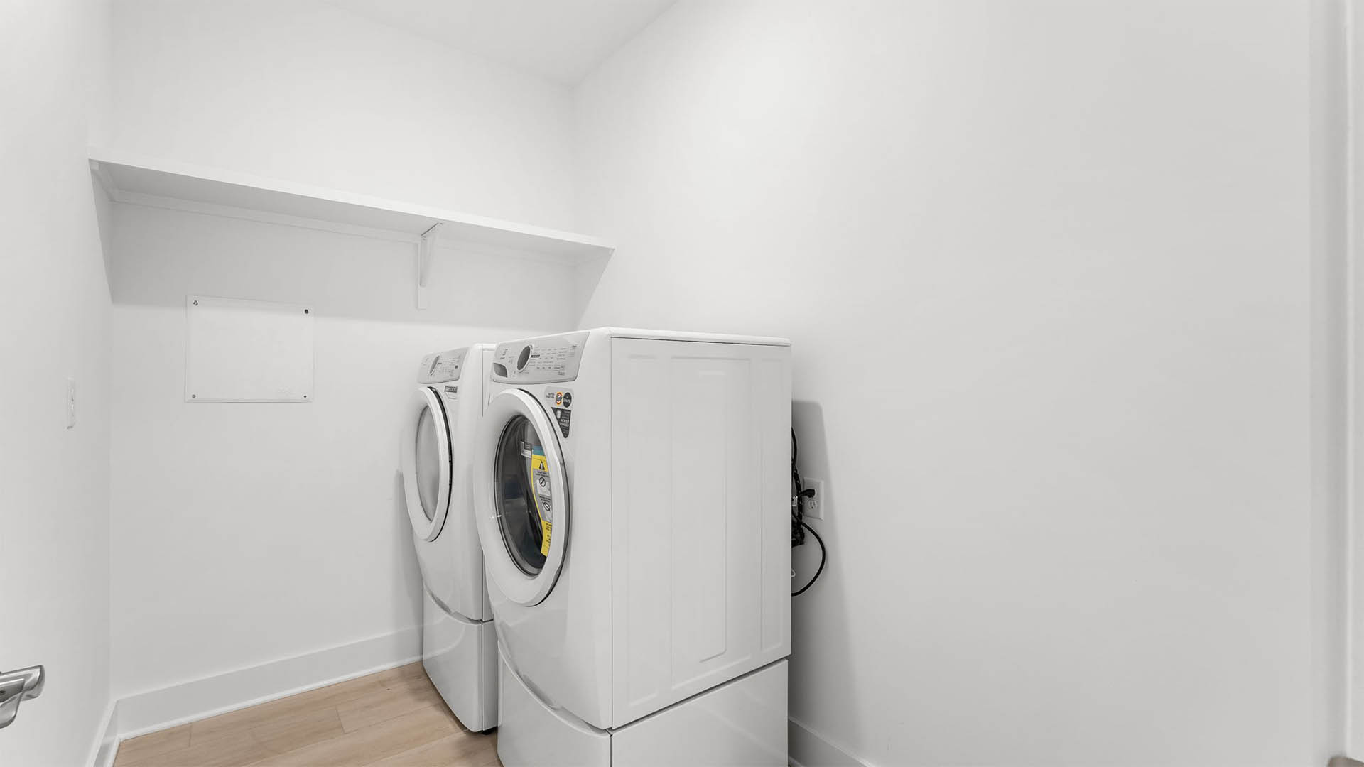 The laundry room has space for a full size washer and dryer and upper wood shelf