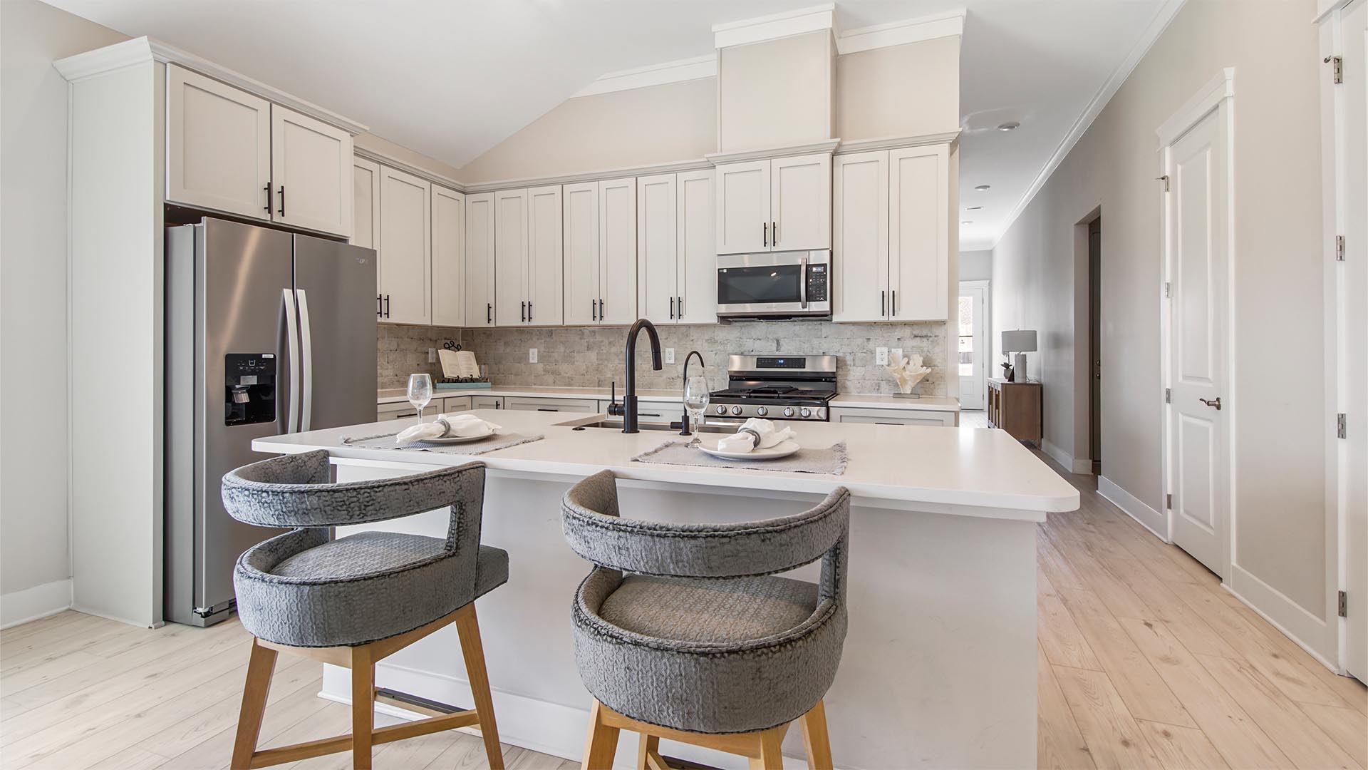 Open concept kitchen with plenty of cabinets and kitchen island with bar seating and quartz countertops and tile backsplash.