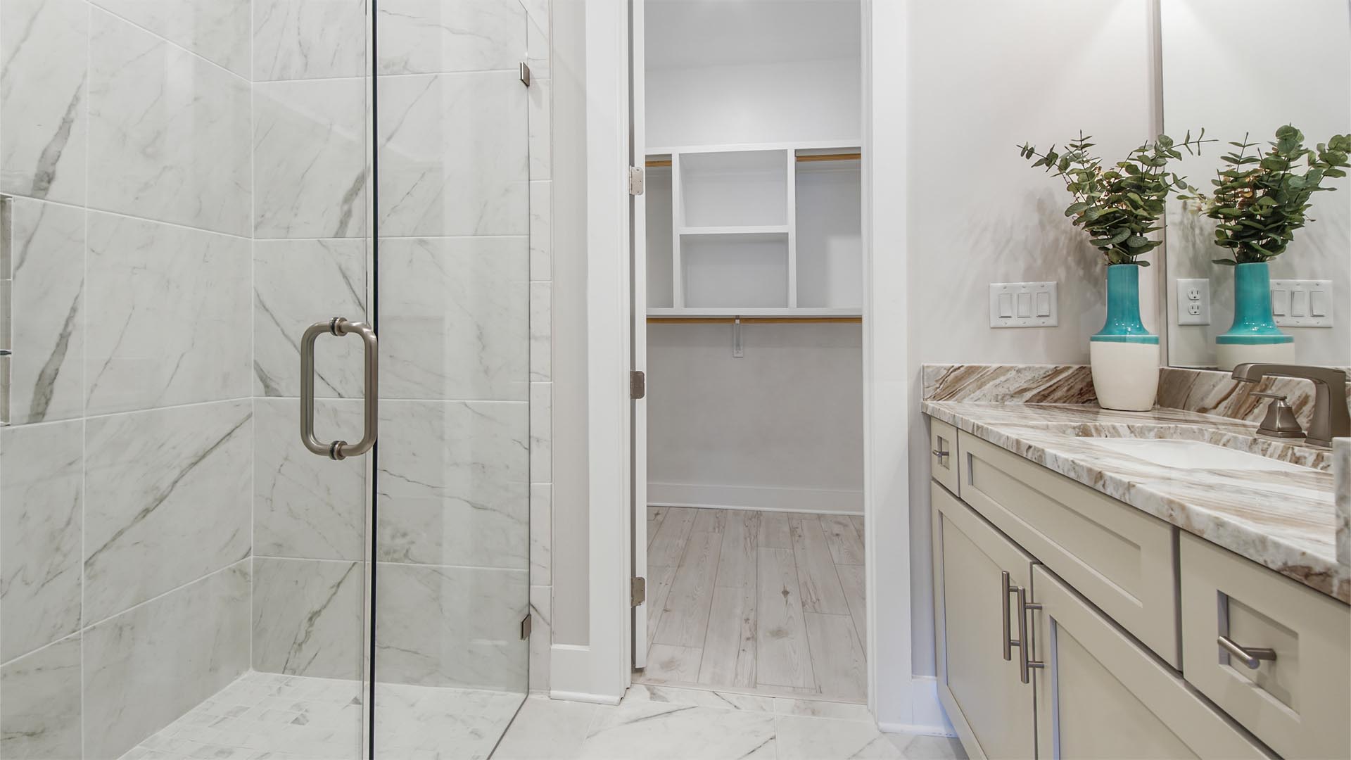 Primary bathroom with tile flooring and two single vanities with quartz countertops and walk-in closet with wood shelving.