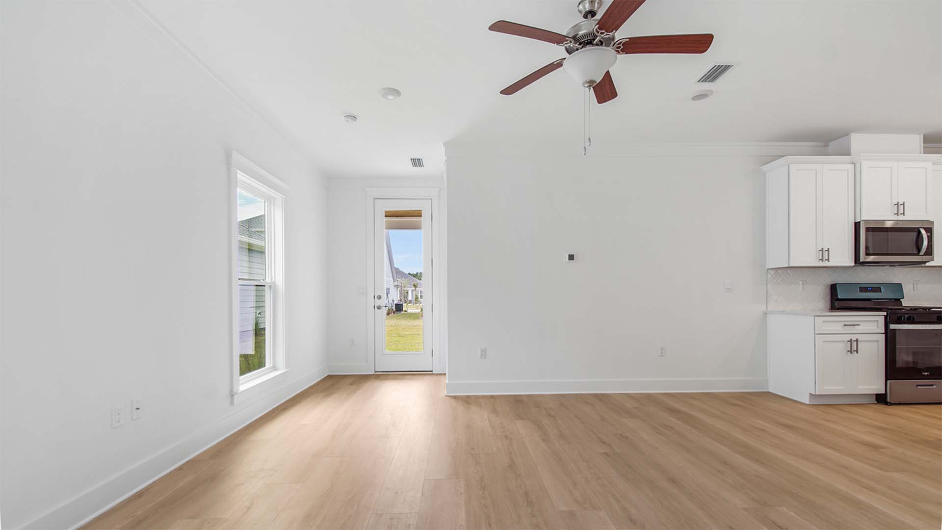Open living area with EVP flooring and ceiling fan and large window and glass back door to covered patio.