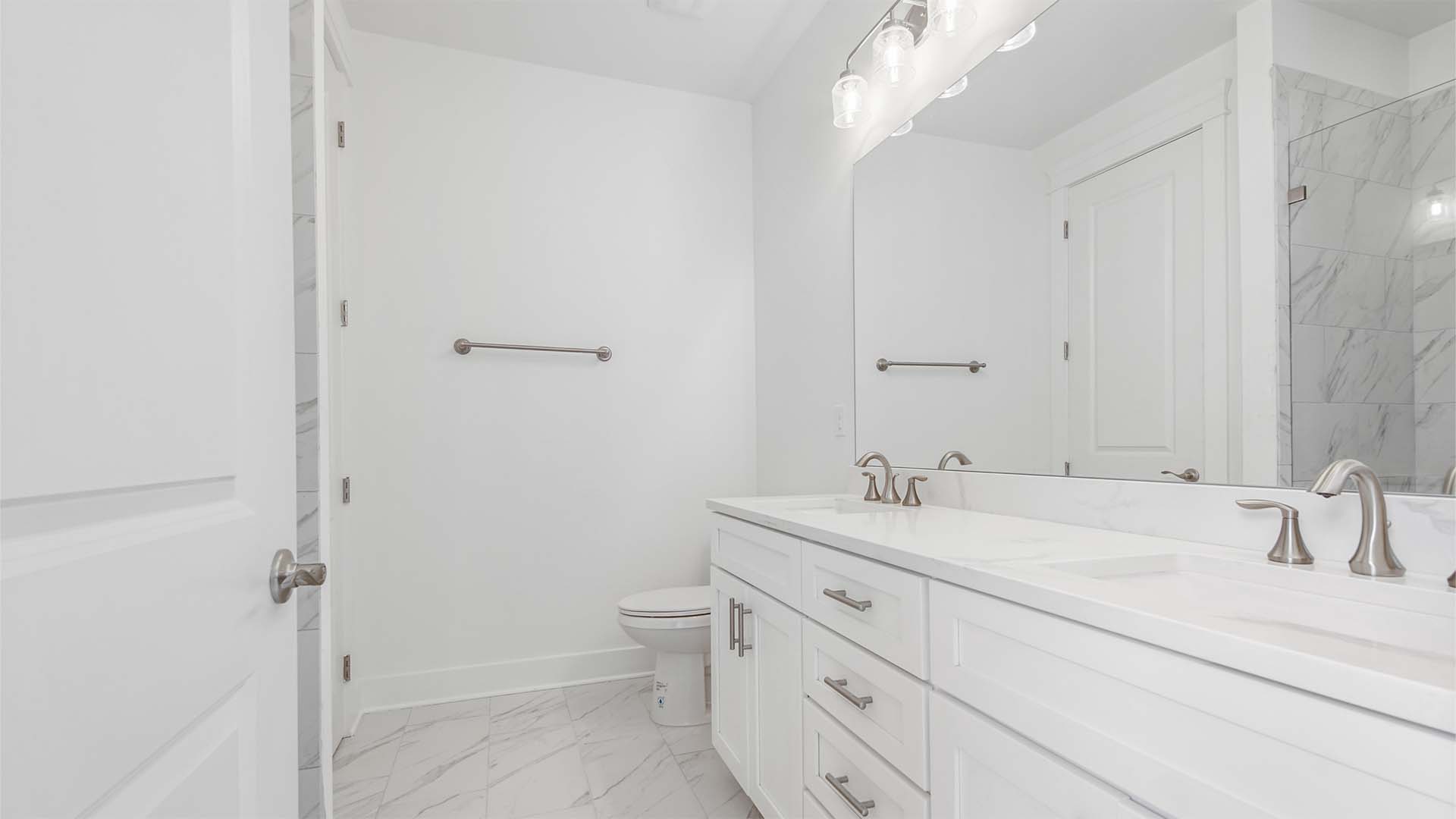 Primary bathroom with dual vanity and quartz countertops and white cabinetry and white marbled tile flooring.