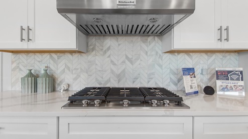 A elegant tile backsplash compliments the white cabinetry and gas cooktop stove