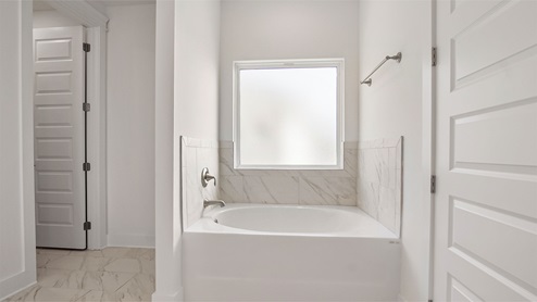 Primary bathroom with large soaking tub and marbled tile shower below frosted glass window.