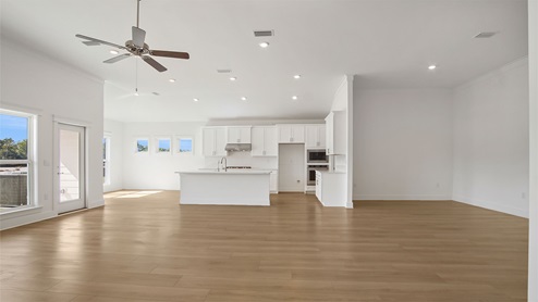 Opening living area with EVP flooring and large windows and ceiling fan and open kitchen next to breakfast nook.