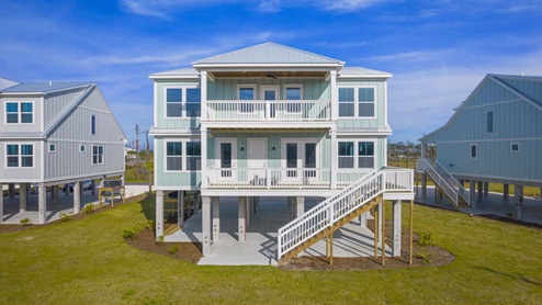 Two story home on pilings with 2 balconies and staircase and yard.