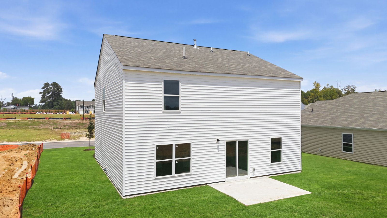 rear view of two story home with back patio pad and yard