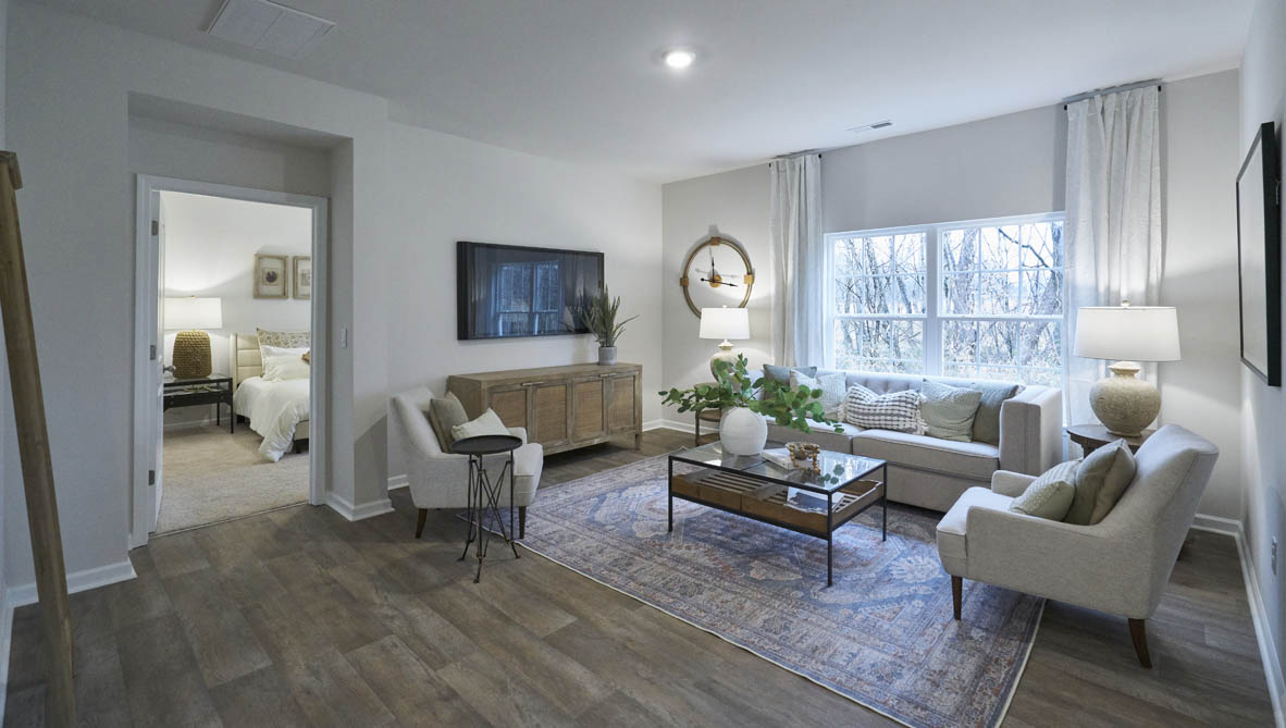 Spacious living room with brown flooring, white walls and windows