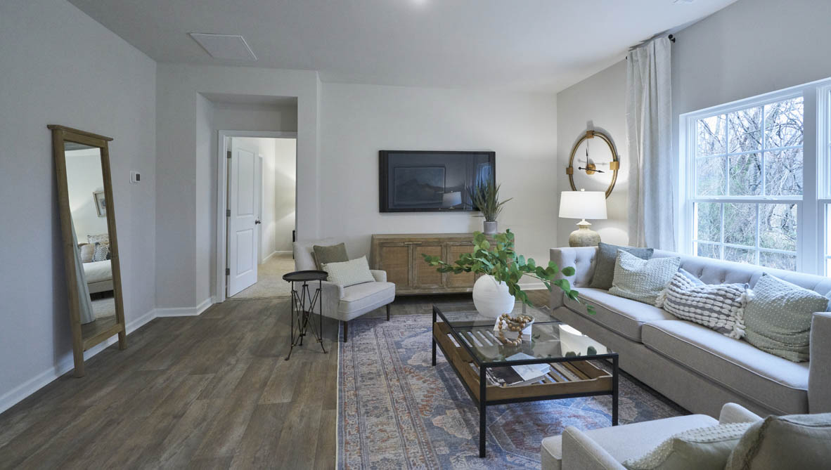 Spacious living room with brown flooring, white walls and windows