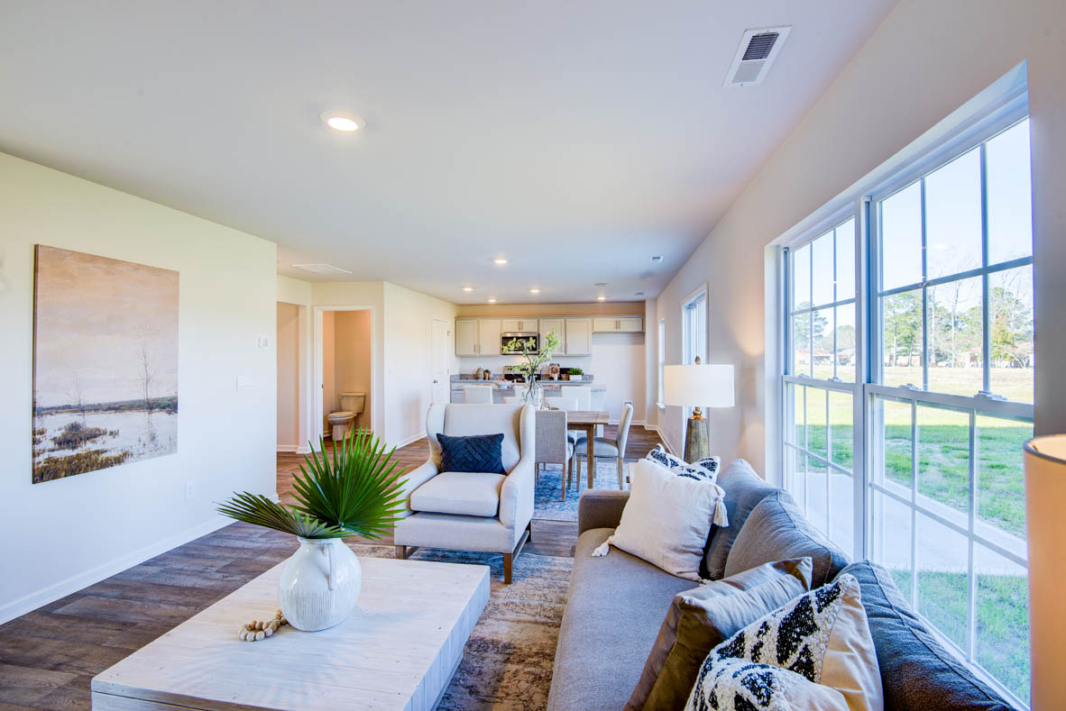 Spacious living room with brown flooring, white walls and windows