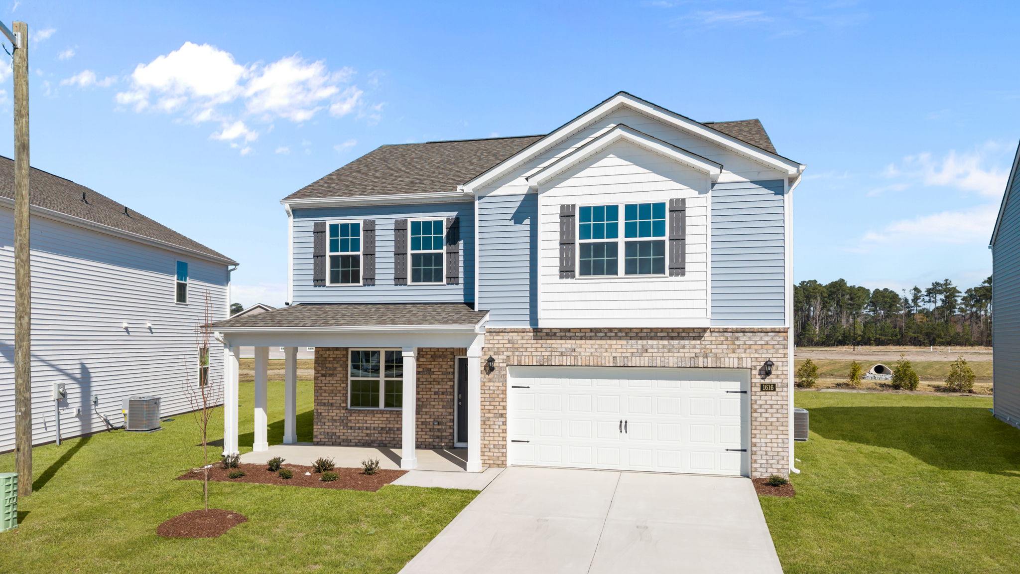 Two story brick and blue home with paved driveway and covered front porch