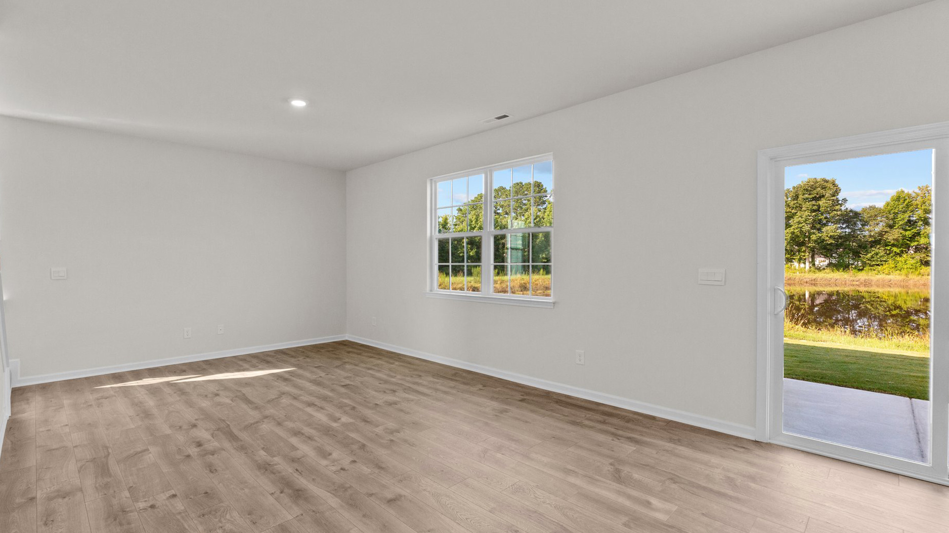 Spacious living room with brown flooring, white walls and windows