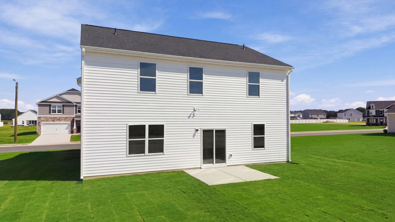 rear view of two story white home with back patio pad
