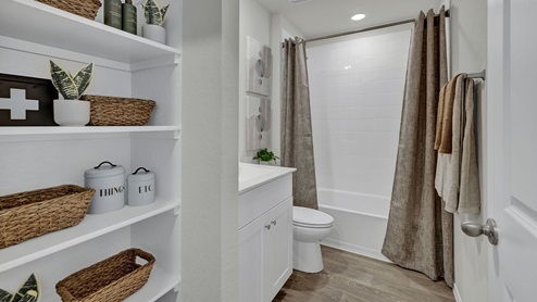 Hall bath with wooden shelving, toilet, and tub.