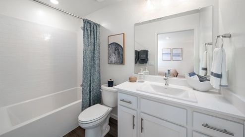 Interior photo of a guest bathroom with white counters, white cabinets and a shower