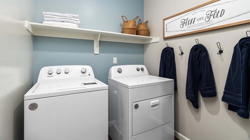 Interior photo of a laundry room with a washer, dryer, and storage shelf.