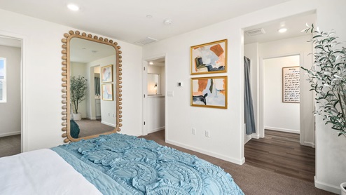 Interior photo of primary bedroom with a bed, large mirror on the wall, and an entry way to the ensuite bathroom