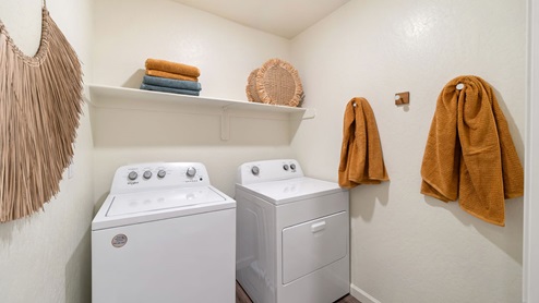 Interior photo of a laundry room with a washer, dryer, and storage shelf