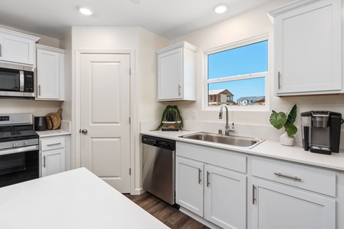 Interior photo of kitchen with white cabinets, white countertops, stainless steel appliances, and window above sink.
