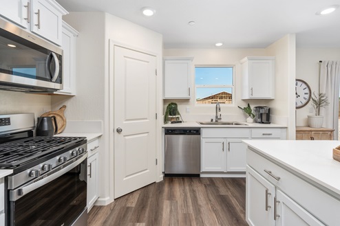 Interior photo of kitchen with white cabinets, white countertops, stainless steel appliances, and window above sink.