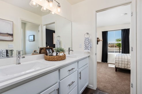 Interior photo of Jack and Jill bathroom with white countertops, white cabinets, and large mirror.