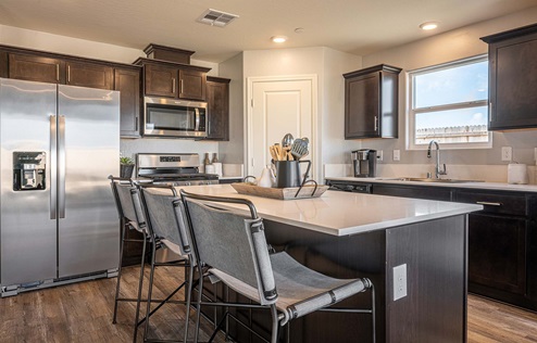 Interior photo of kitchen with dark brown cabinets, white countertops, and stainless steel appliances.
