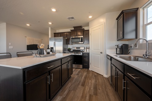 Interior photo of kitchen with dark brown cabinets, white countertops, and stainless steel appliances.