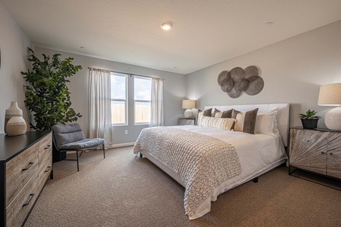 Interior photo of primary suite with bed, dresser, and large windows.