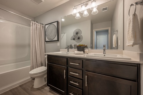 Interior photo of primary bathroom with dark brown cabinets, white countertops, shower, and large mirror.
